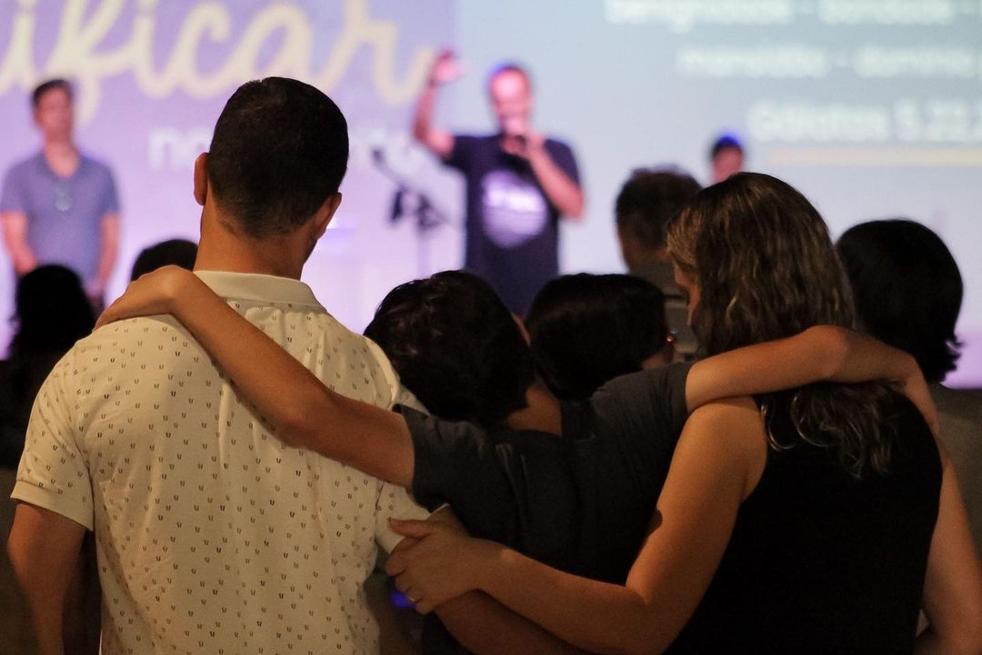 Família de três pessoas se abraçando durante um culto